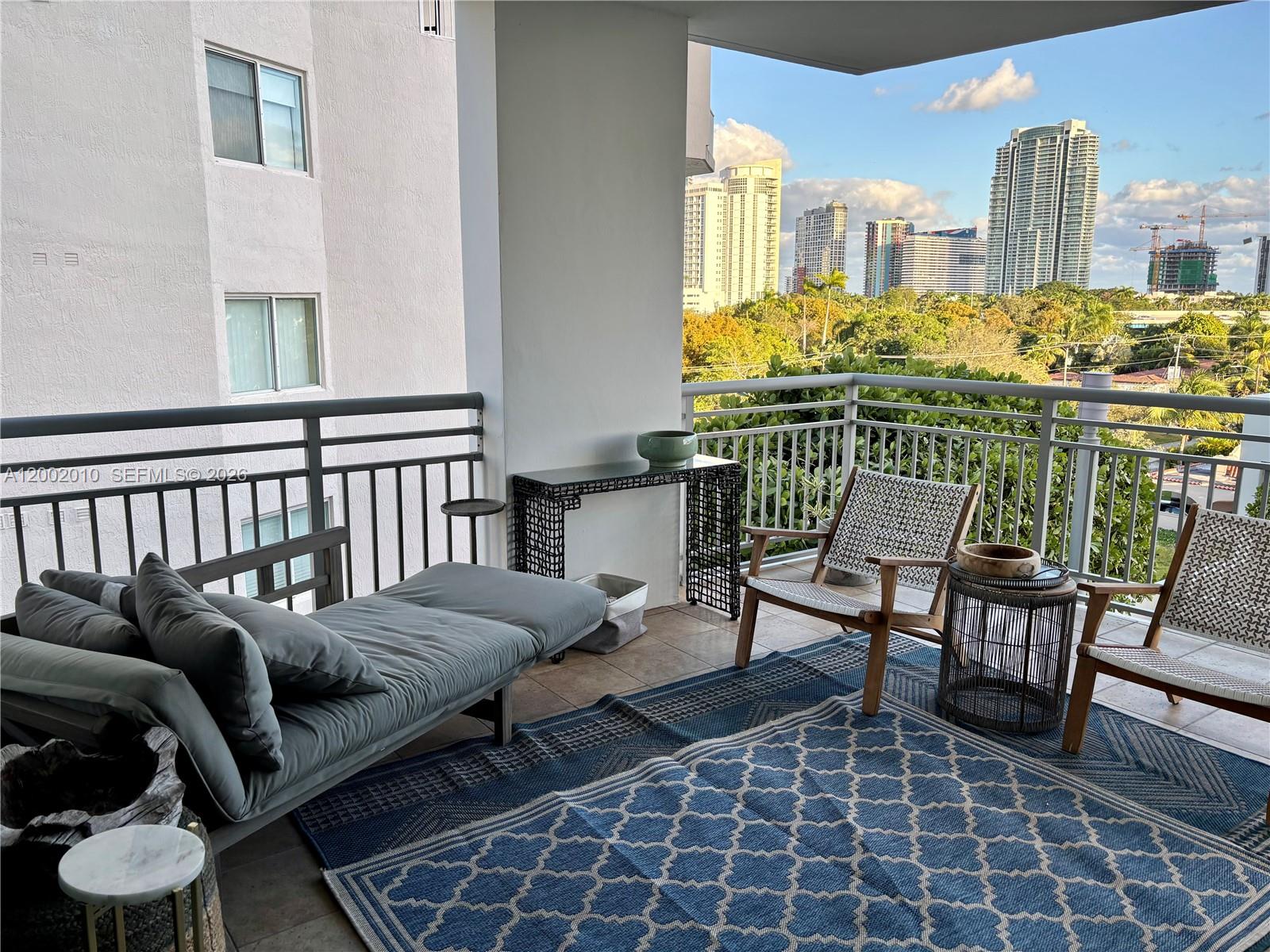 A balcony features a gray daybed, two chairs, a patterned rug, and city skyline views — 2021 SW 3rd Ave # 605, Miami FL 33129, MIAMI, FL