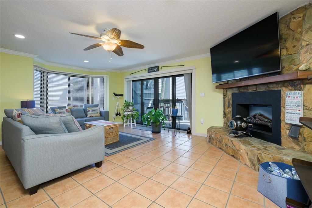 A living room features a stone fireplace, tile flooring, a ceiling fan, and sliding doors — 4421 S ATLANTIC AVENUE UNIT A2, PONCE INLET, FL