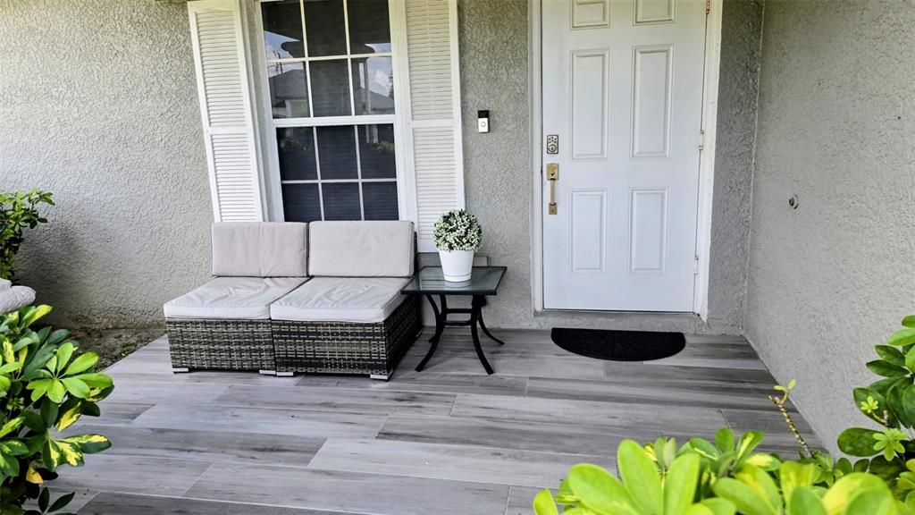 A front porch features gray wood-look tile flooring, a wicker loveseat, and a white door — 706 NW 1ST LANE, CAPE CORAL, FL
