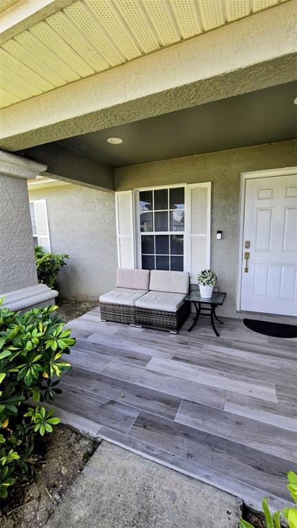 A covered front porch features gray wood-look tile flooring, a wicker loveseat, and a white door — 706 NW 1ST LANE, CAPE CORAL, FL