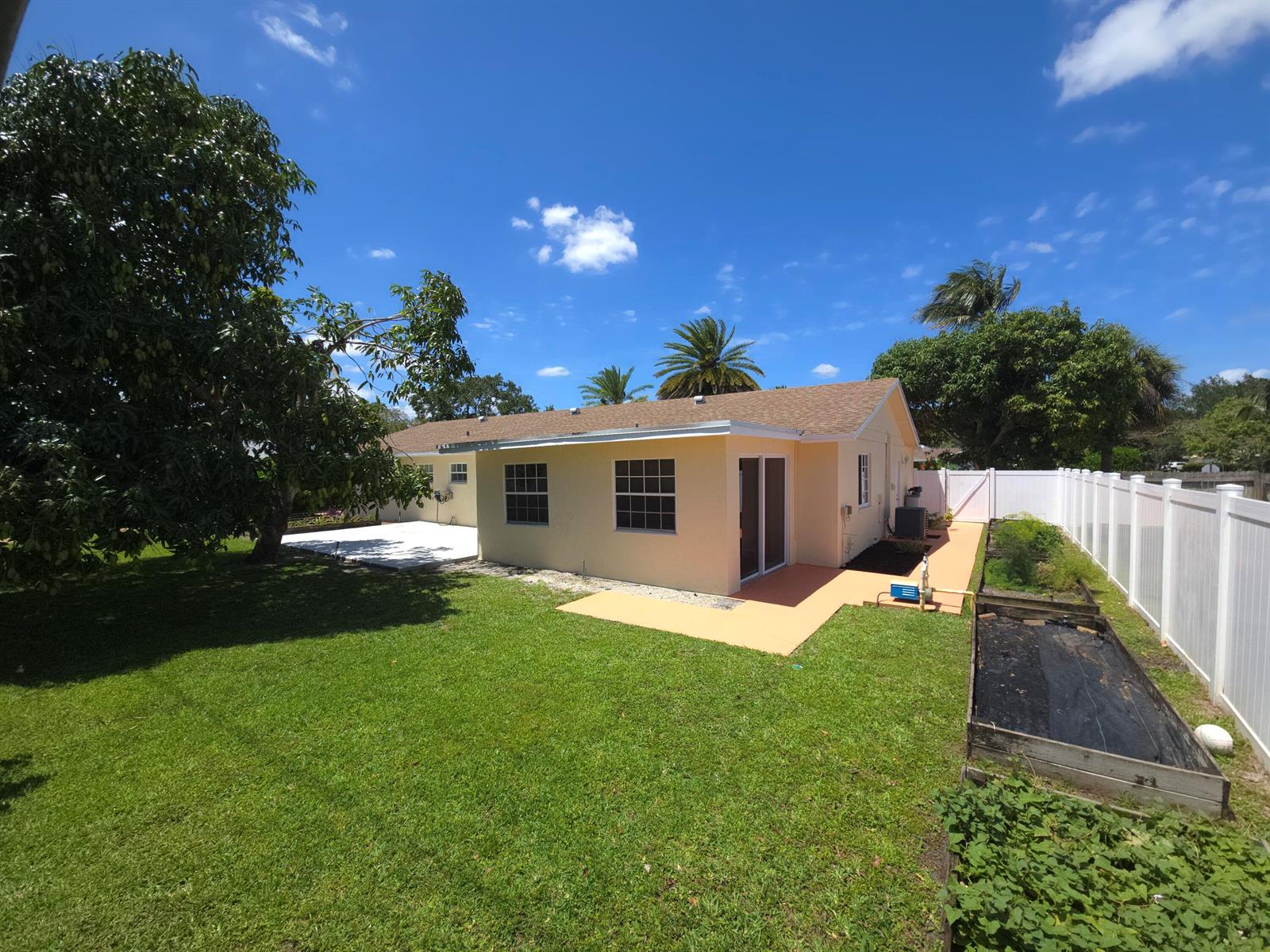 A backyard view of a single-story house with a patio, lawn, and white vinyl fence — 4554 Franwood Drive, Delray Beach FL 33445, DELRAY BEACH, FL