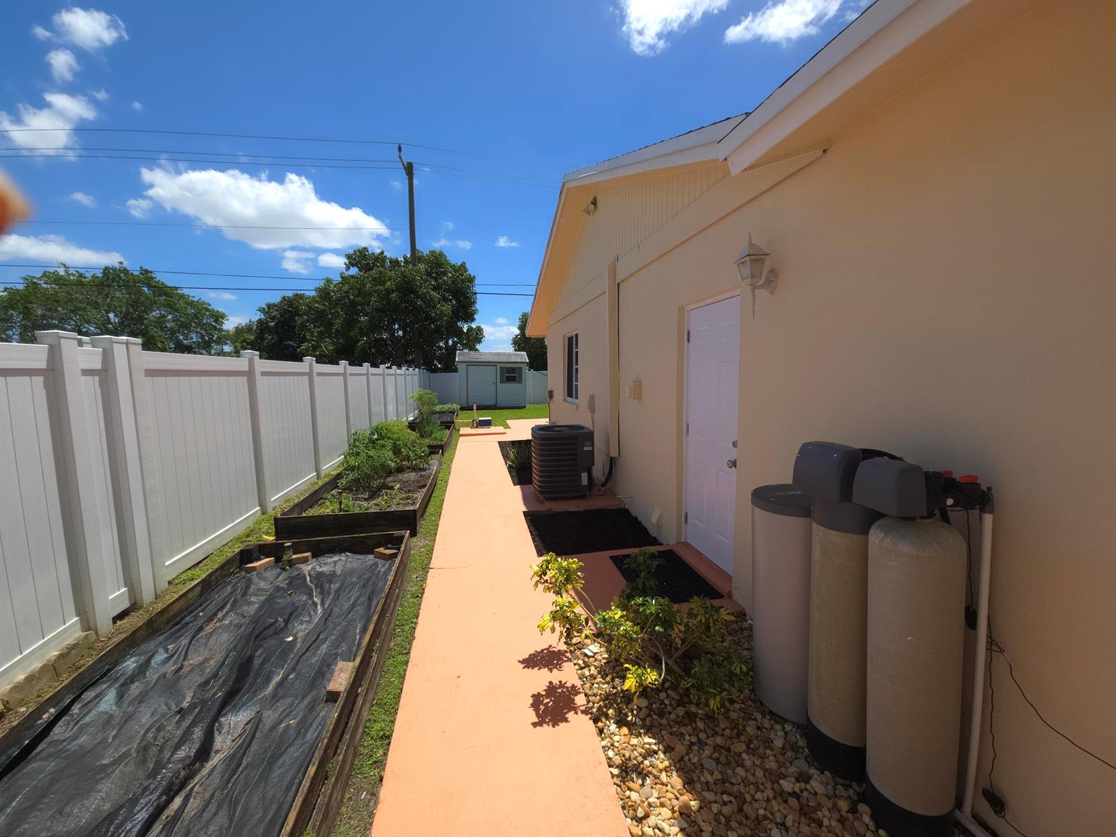 A side yard features a concrete walkway, raised garden beds, and exterior water filtration tanks — 4554 Franwood Drive, Delray Beach FL 33445, DELRAY BEACH, FL