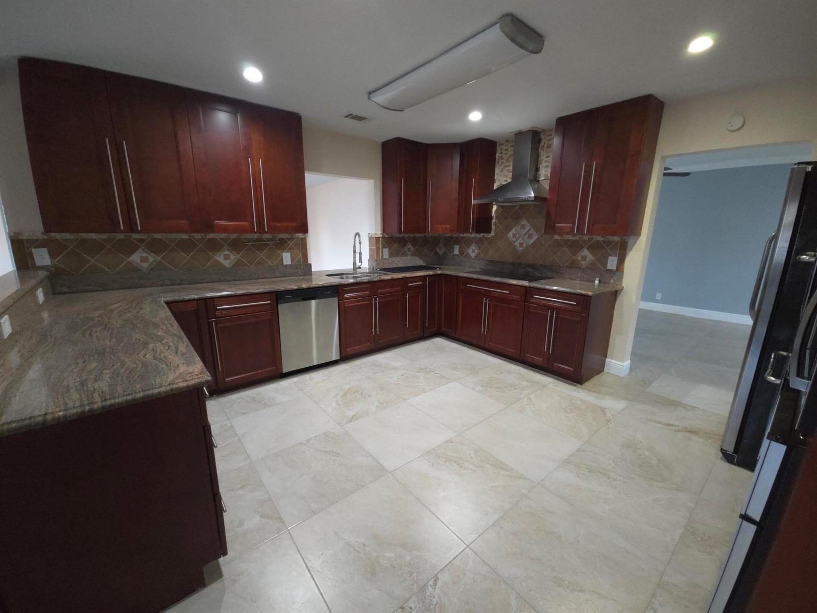 A kitchen features dark wood cabinets, granite countertops, stainless steel appliances, and light tile flooring — 4554 Franwood Drive, Delray Beach FL 33445, DELRAY BEACH, FL