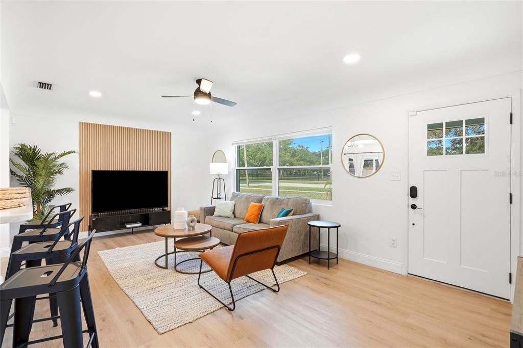 A living room features light wood flooring, a slatted wood accent wall, and a white door — 2117 N HERCULES AVENUE, CLEARWATER, FL