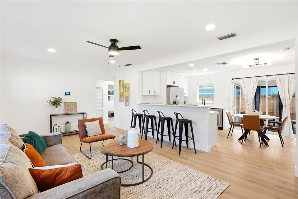 An open-concept living room and kitchen featuring white cabinetry, a breakfast bar, and wood flooring — 2117 N HERCULES AVENUE, CLEARWATER, FL