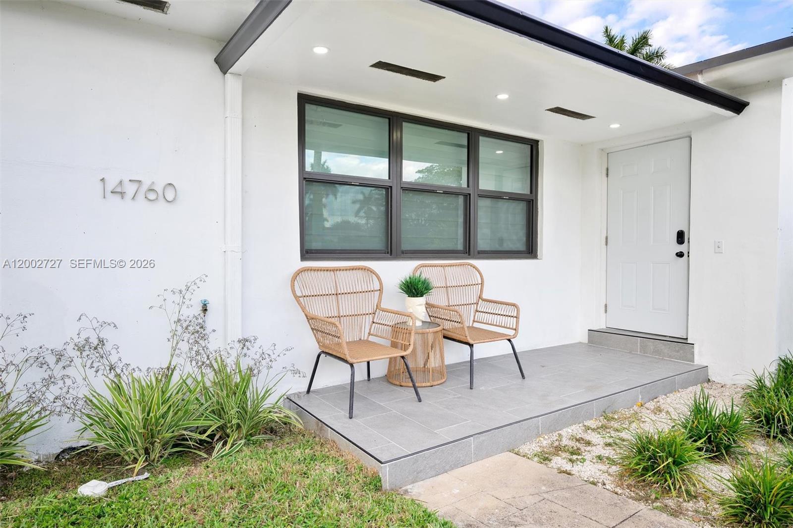 A white house exterior features a tiled front porch with two wicker chairs and table — 14760 S Spur Dr, Miami FL 33161, MIAMI, FL