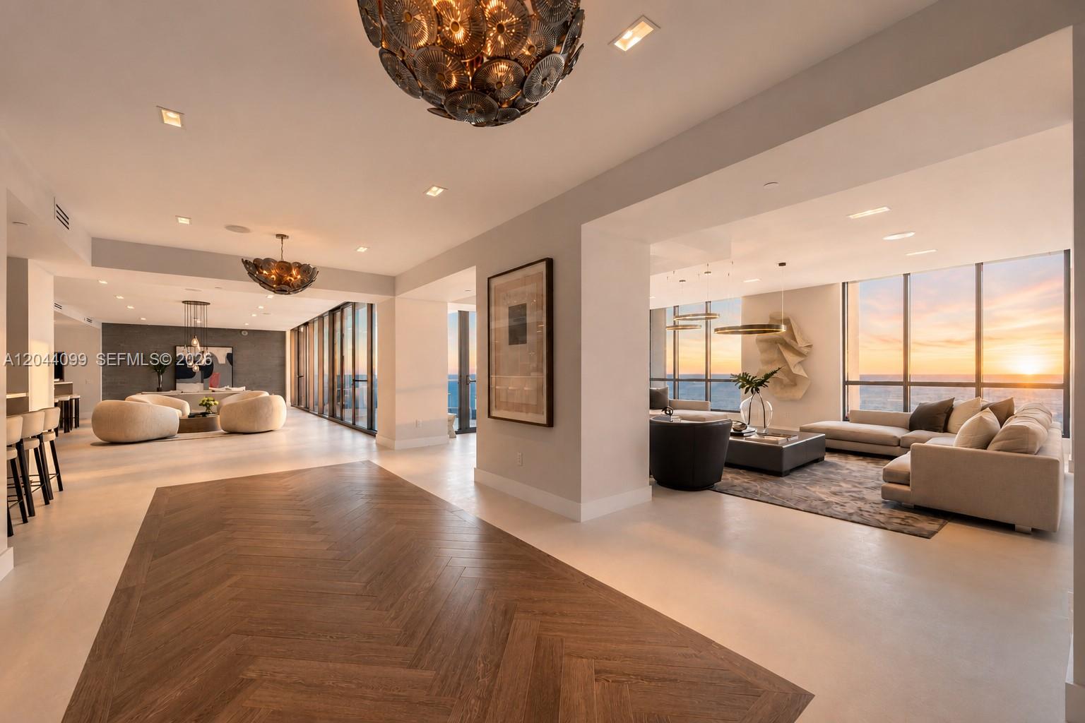 A spacious, modern living area features herringbone wood flooring, neutral furniture, and floor-to-ceiling ocean views — 5959 Collins Ave, Miami Beach FL 33140, MIAMI BEACH, FL
