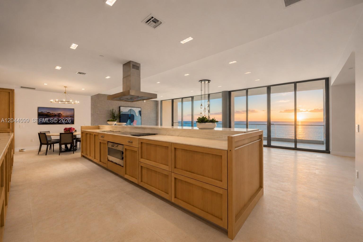 A modern kitchen features a large wooden island, stainless steel appliances, and floor-to-ceiling ocean views — 5959 Collins Ave, Miami Beach FL 33140, MIAMI BEACH, FL