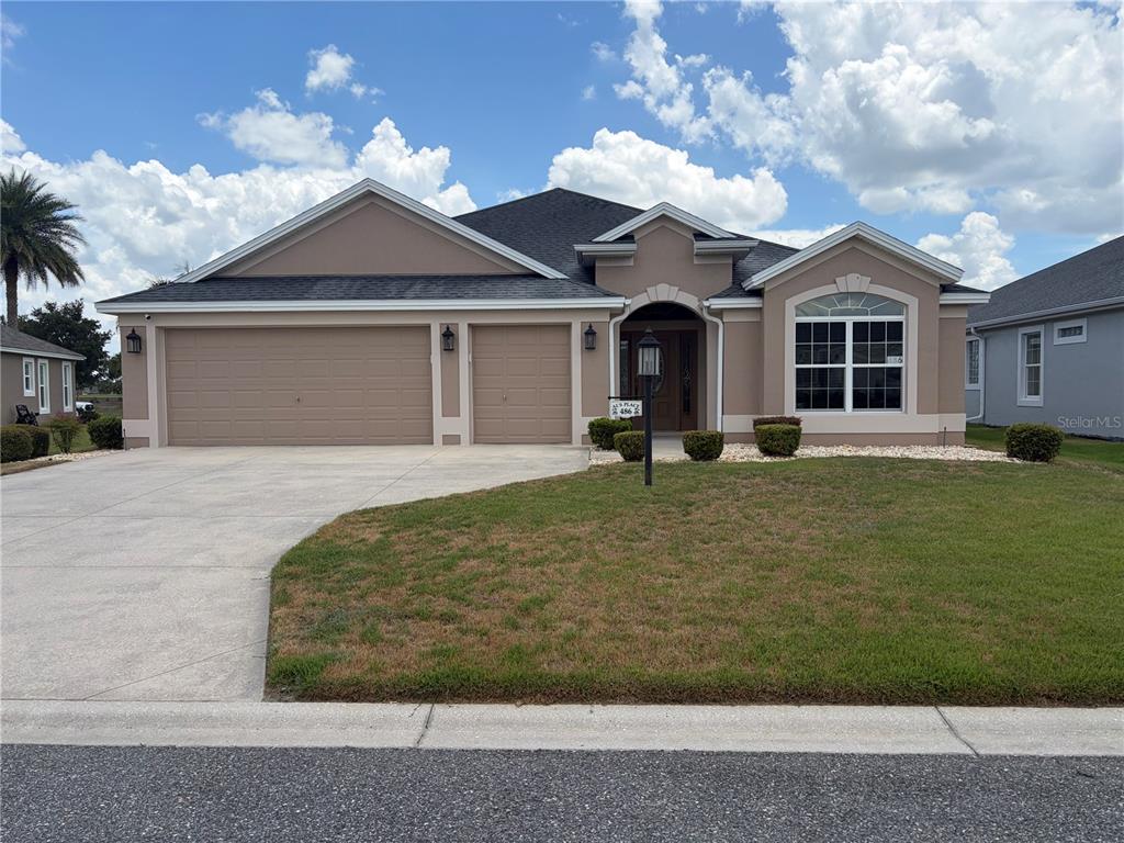 A tan single-story house with a three-car garage and a front lawn under a blue sky — 486 INDEPENDENCE PATH, THE VILLAGES, FL