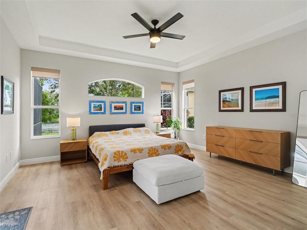 A bedroom features a bed, dresser, ceiling fan, and large windows with a water view — 14146 CATTLE EGRET PL, LAKEWOOD RANCH, FL