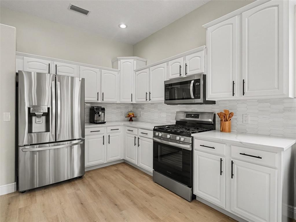 A modern kitchen features white cabinets, stainless steel appliances, and light wood-look flooring — 14146 CATTLE EGRET PL, LAKEWOOD RANCH, FL