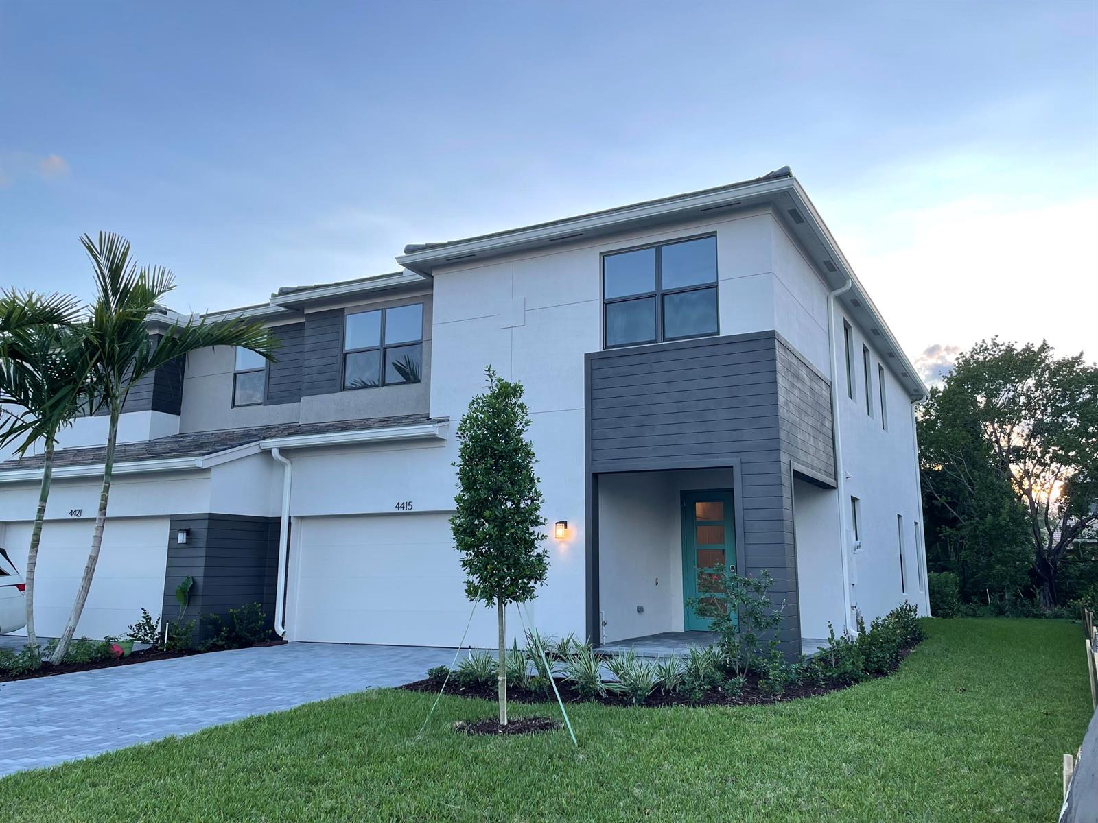 A two-story townhouse features white stucco walls, dark gray horizontal siding, and a teal front door — 4415 Arcturus Lane, Lake Worth FL 33467, LAKE WORTH, FL