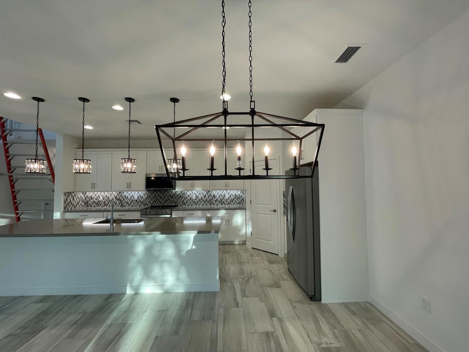 A kitchen with a large island, pendant lighting, a rectangular chandelier, and light wood flooring — 4415 Arcturus Lane, Lake Worth FL 33467, LAKE WORTH, FL