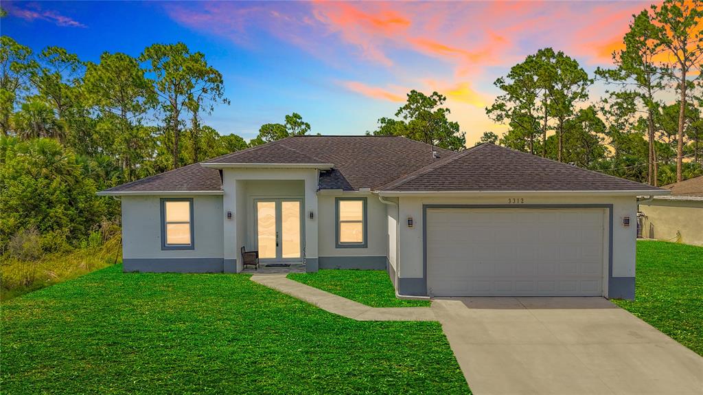 A single-story house with a two-car garage and a concrete walkway under a sunset sky — 3312 72ND STREET W, LEHIGH ACRES, FL