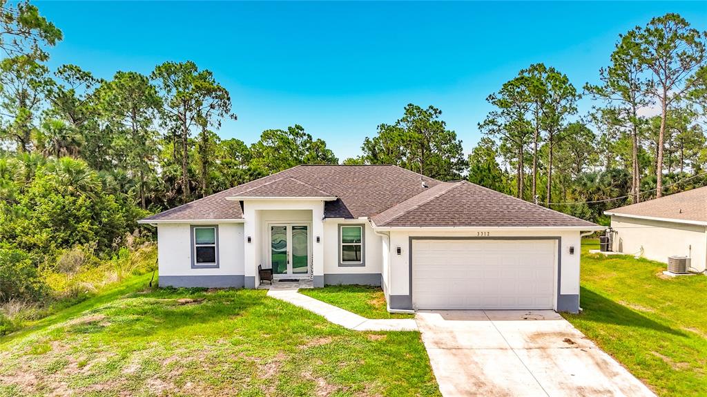 A single-story white house with a two-car garage sits on a grassy lot with trees — 3312 72ND STREET W, LEHIGH ACRES, FL