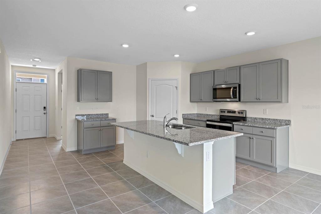 A kitchen features gray cabinets, granite countertops, a center island with a sink, and tile flooring — 5395 CLOUDBERRY AVENUE, LAKELAND, FL