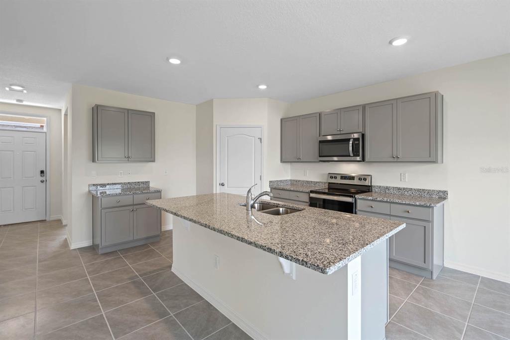 A kitchen features gray cabinets, granite countertops, a central island with a sink, and tile flooring — 5395 CLOUDBERRY AVENUE, LAKELAND, FL
