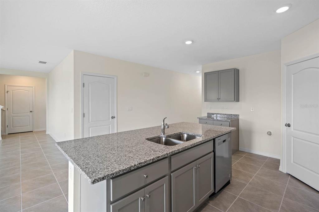 A kitchen island with a granite countertop and gray cabinets sits on a tiled floor — 5395 CLOUDBERRY AVENUE, LAKELAND, FL
