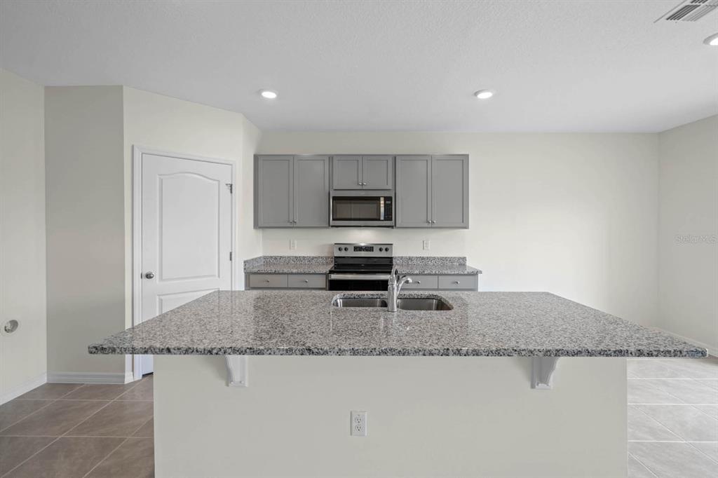 A kitchen features gray cabinets, granite countertops, a central island with a sink, and appliances — 5395 CLOUDBERRY AVENUE, LAKELAND, FL
