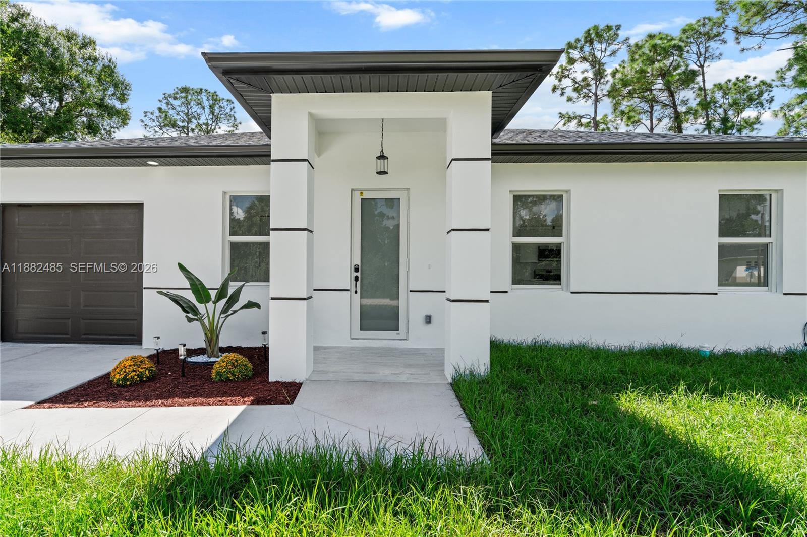 The exterior of a white house features a dark garage door and a covered entryway — 936 Anthony E, Lehigh Acres FL 33974, LEHIGH ACRES, FL