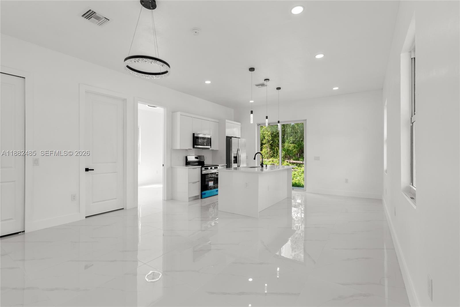 A modern kitchen with white cabinetry and an island sits in an open-concept room — 936 Anthony E, Lehigh Acres FL 33974, LEHIGH ACRES, FL
