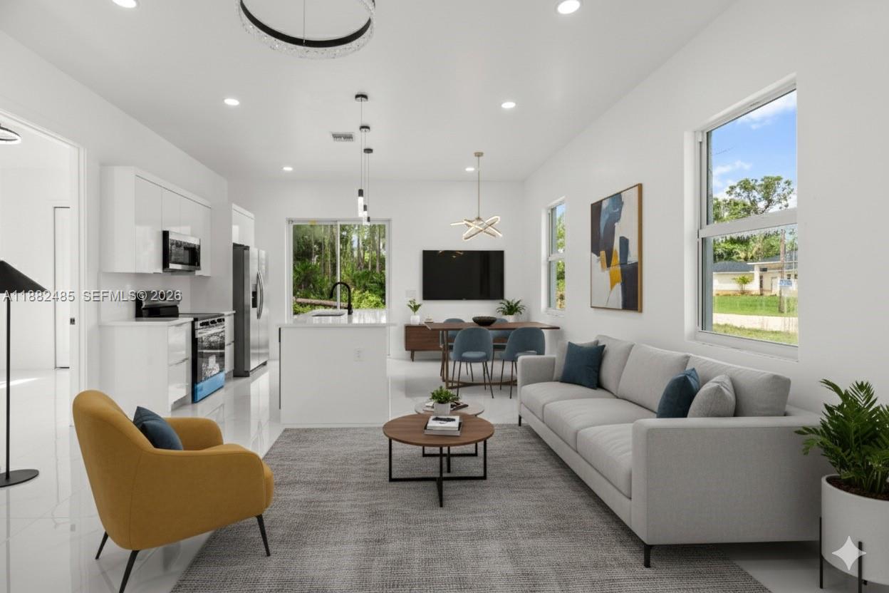 This open-concept living and dining area features white cabinetry, a kitchen island, and modern furniture — 936 Anthony E, Lehigh Acres FL 33974, LEHIGH ACRES, FL