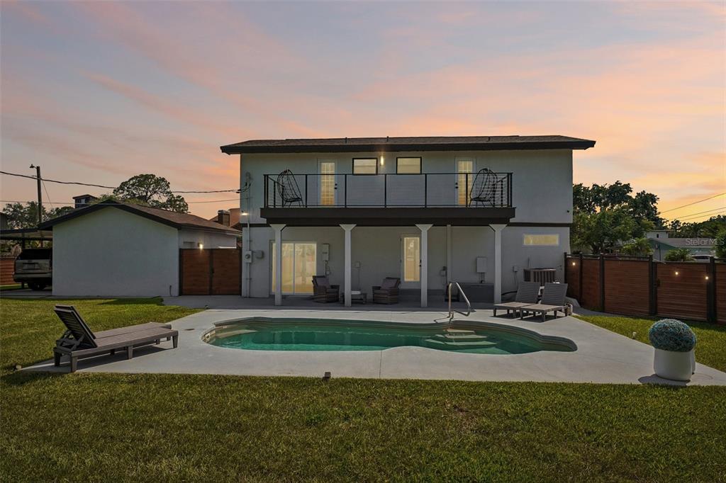 A two-story house with a balcony, a swimming pool, and a fenced backyard at sunset — 5201 HUNTINGTON STREET NE, ST PETERSBURG, FL
