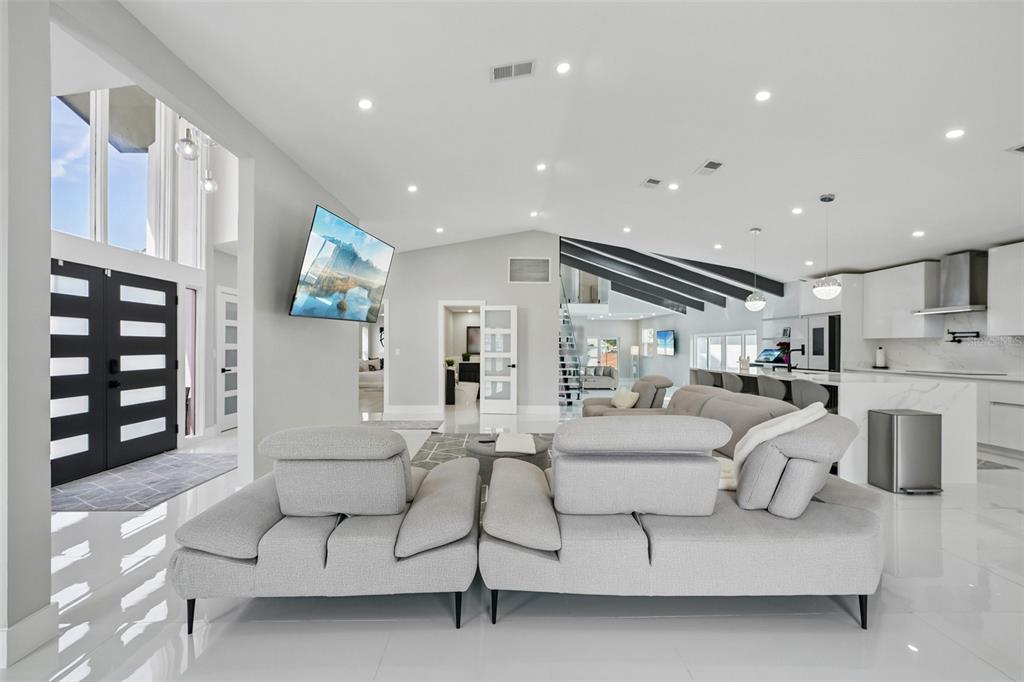 A modern open-concept living room features a large grey sectional, white tile floors, and kitchen — 5201 HUNTINGTON STREET NE, ST PETERSBURG, FL