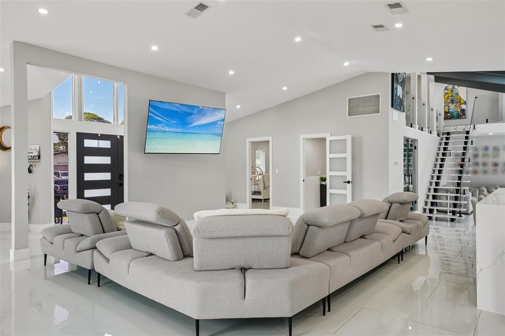 A modern living room features a large grey sectional sofa, a wall-mounted television, and stairs — 5201 HUNTINGTON STREET NE, ST PETERSBURG, FL