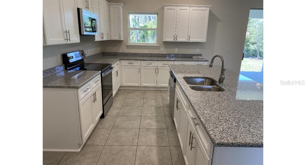 A kitchen features white cabinets, granite countertops, stainless steel appliances, and light tile flooring — 4501 CARRIZAL TERRACE, NORTH PORT, FL