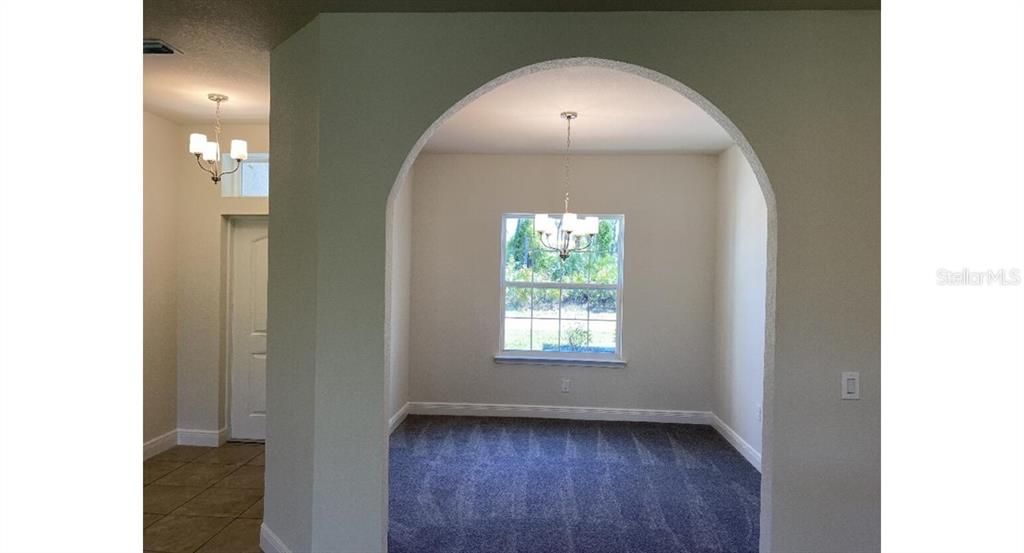 A carpeted dining room is framed by an arched entryway with a central chandelier — 4501 CARRIZAL TERRACE, NORTH PORT, FL