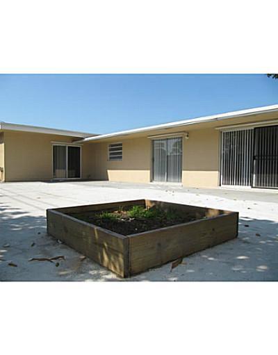 A raised wooden garden bed sits on a concrete patio outside a beige house — 1370 NW 54th Terrace, Lauderhill FL 33313, LAUDERHILL, FL