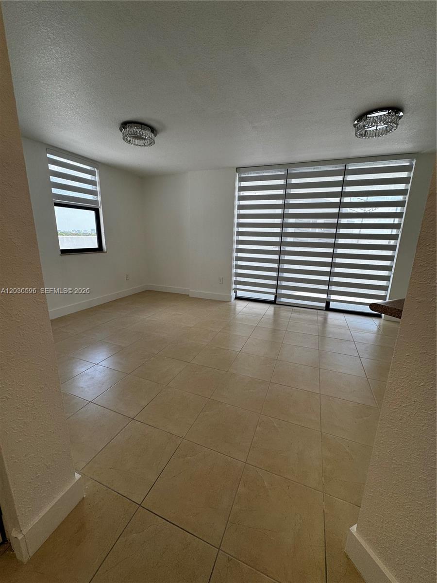 An empty room features beige tile flooring, white walls, two ceiling lights, and striped blinds — 2301 SW 27th Ave # 503, Miami FL 33145, MIAMI, FL