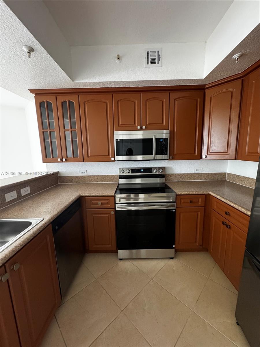 A kitchen features brown wooden cabinets, stainless steel appliances, and tan countertops — 2301 SW 27th Ave # 503, Miami FL 33145, MIAMI, FL