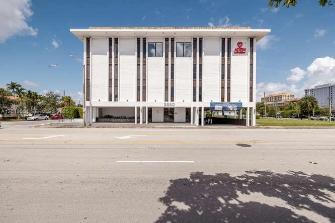 A four-story white commercial building with vertical window columns stands along a paved road — 2850 S Douglas Rd, Coral Gables FL 33134, CORAL GABLES, FL