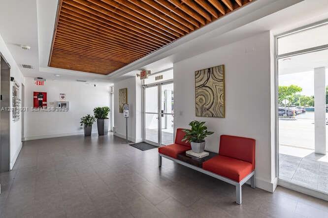 A modern lobby features a slatted wood ceiling, red bench seating, and glass entry doors — 2850 S Douglas Rd, Coral Gables FL 33134, CORAL GABLES, FL