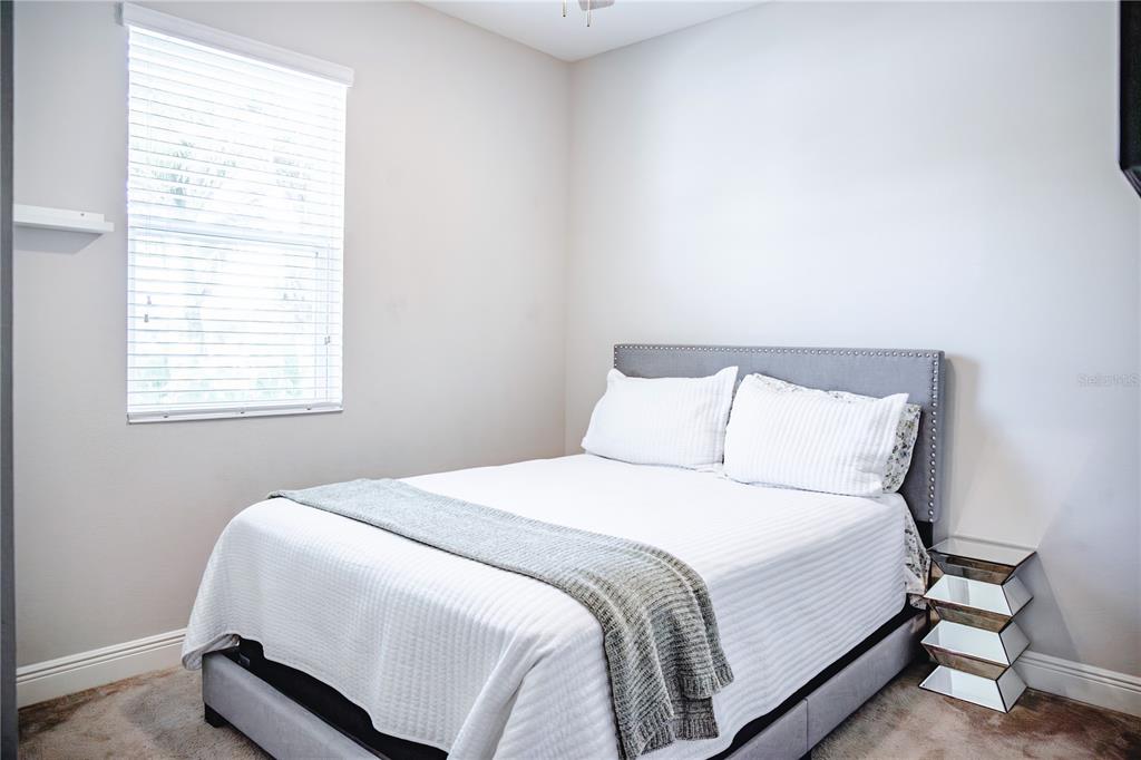 A bedroom features a gray upholstered bed, white bedding, and a mirrored nightstand — 10452 LAGUNA PLAINS DRIVE, RIVERVIEW, FL