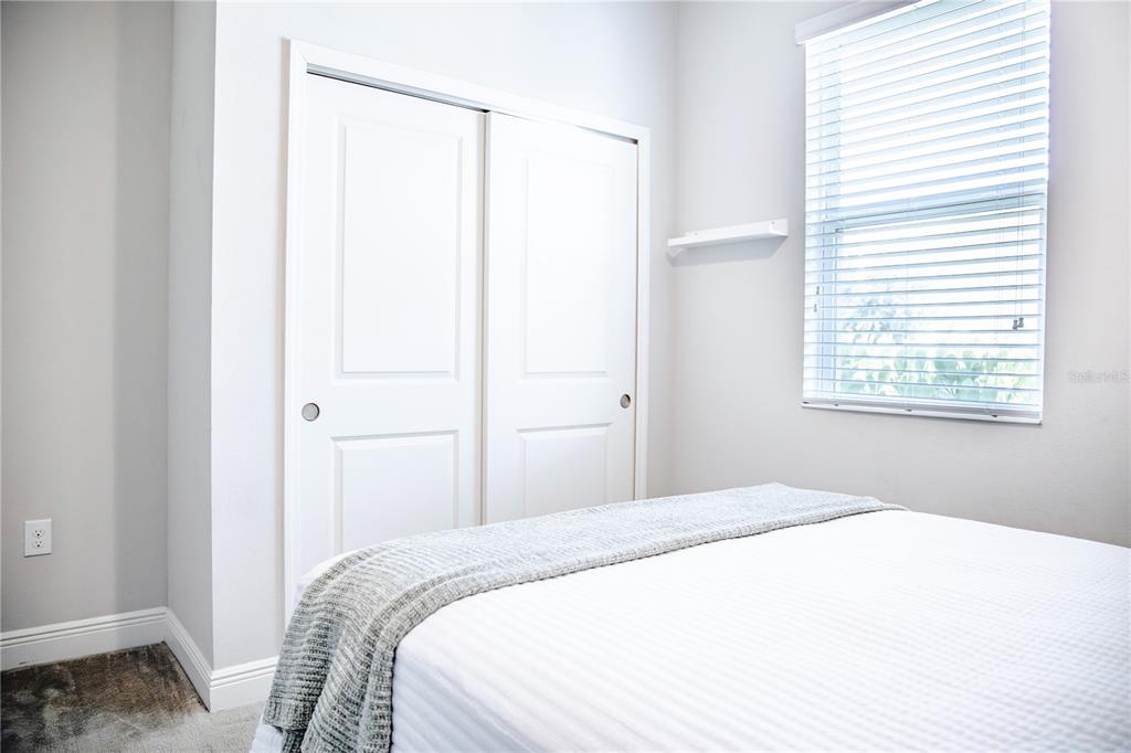 A bedroom features a white bed, sliding closet doors, and a window with blinds — 10452 LAGUNA PLAINS DRIVE, RIVERVIEW, FL