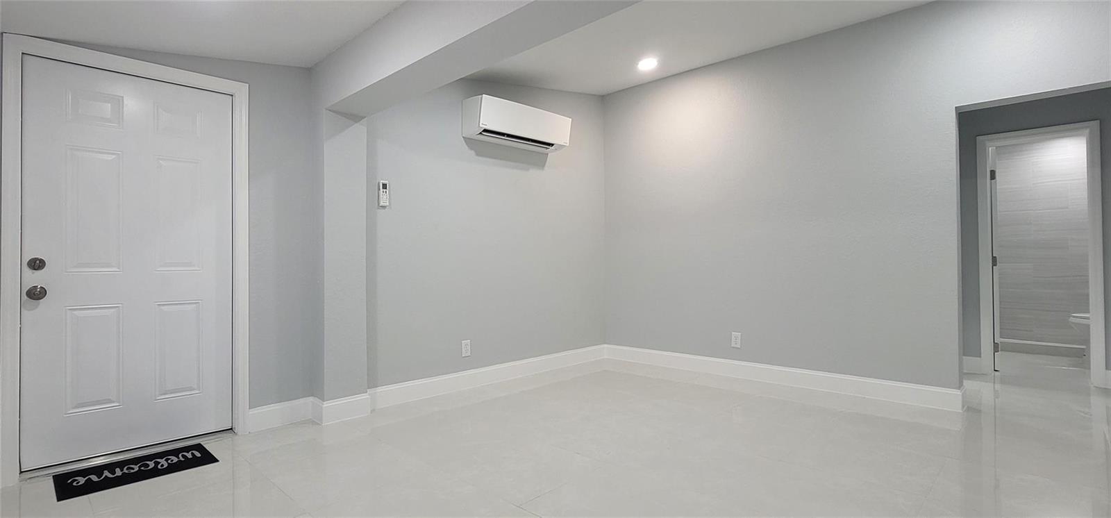 A minimalist room features light gray walls, white trim, tile flooring, and a wall-mounted AC — 4365 27th Avenue, Vero Beach FL 32967, VERO BEACH, FL