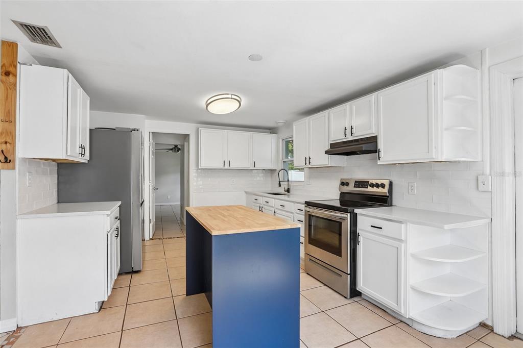A kitchen features white cabinets, a blue island with a wood top, and tile flooring — 8090 68TH STREET N, PINELLAS PARK, FL