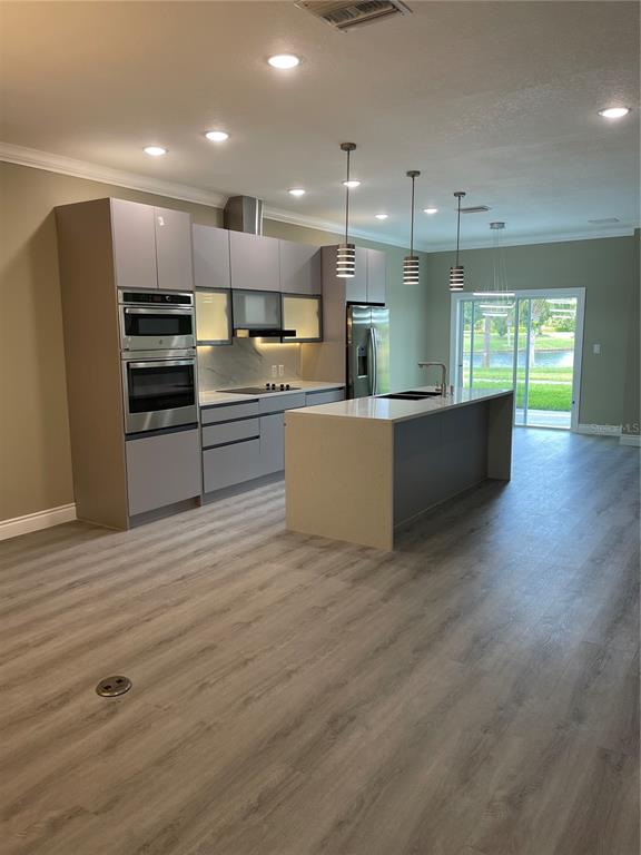 A modern kitchen features gray flat-panel cabinetry, a central island, and light wood-look flooring — 1810 BRENTWOOD COURT, DAVENPORT, FL