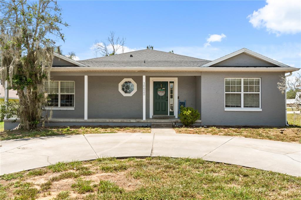 A gray single-story house features a covered front porch, a dark green door, and a driveway — 10022 CAROLE PLACE, LEESBURG, FL