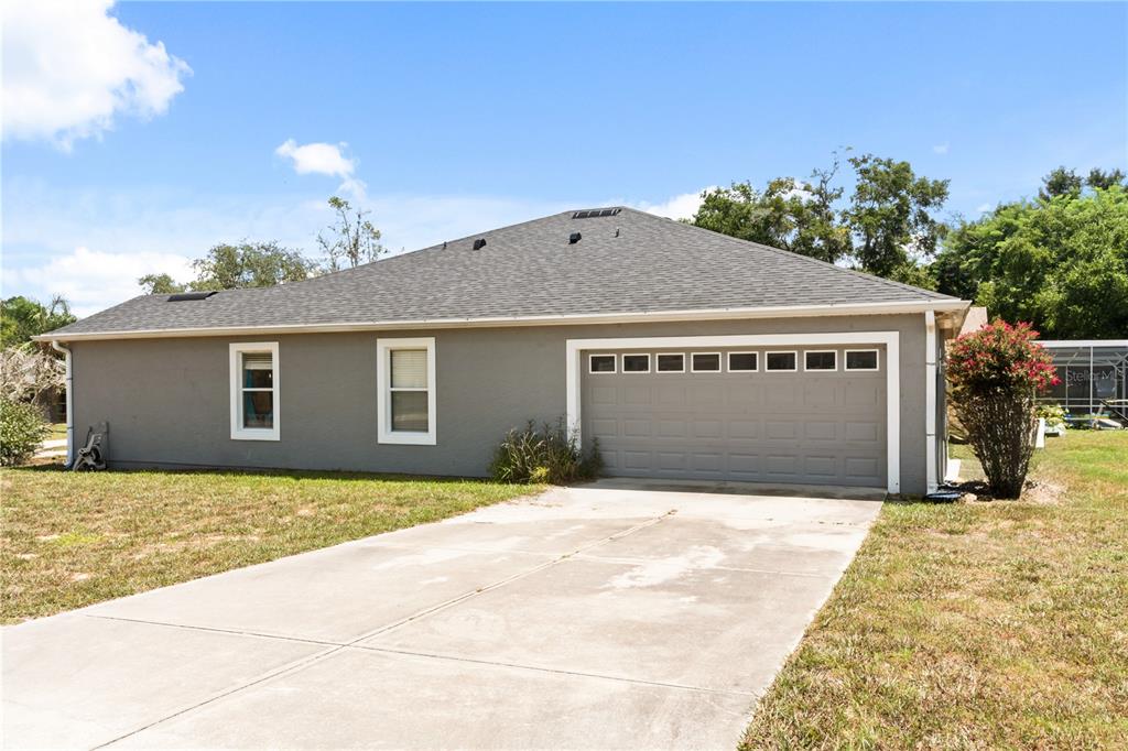 A gray single-story house features a two-car garage, white trim, and a concrete driveway — 10022 CAROLE PLACE, LEESBURG, FL