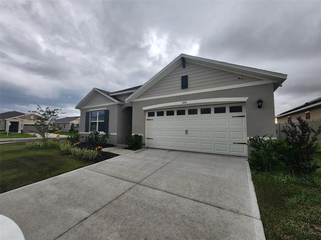 A single-story house with a gray stucco exterior, a two-car garage, and a concrete driveway — 1051 GRIFFON AVENUE, LAKE ALFRED, FL
