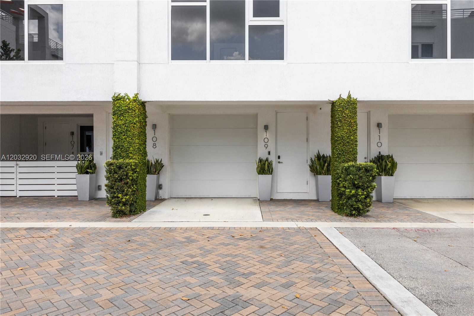 The exterior view shows three adjacent townhome units with white walls, garage doors, and vertical landscaping — 455 NE 39th St # 109, Miami FL 33137, MIAMI, FL