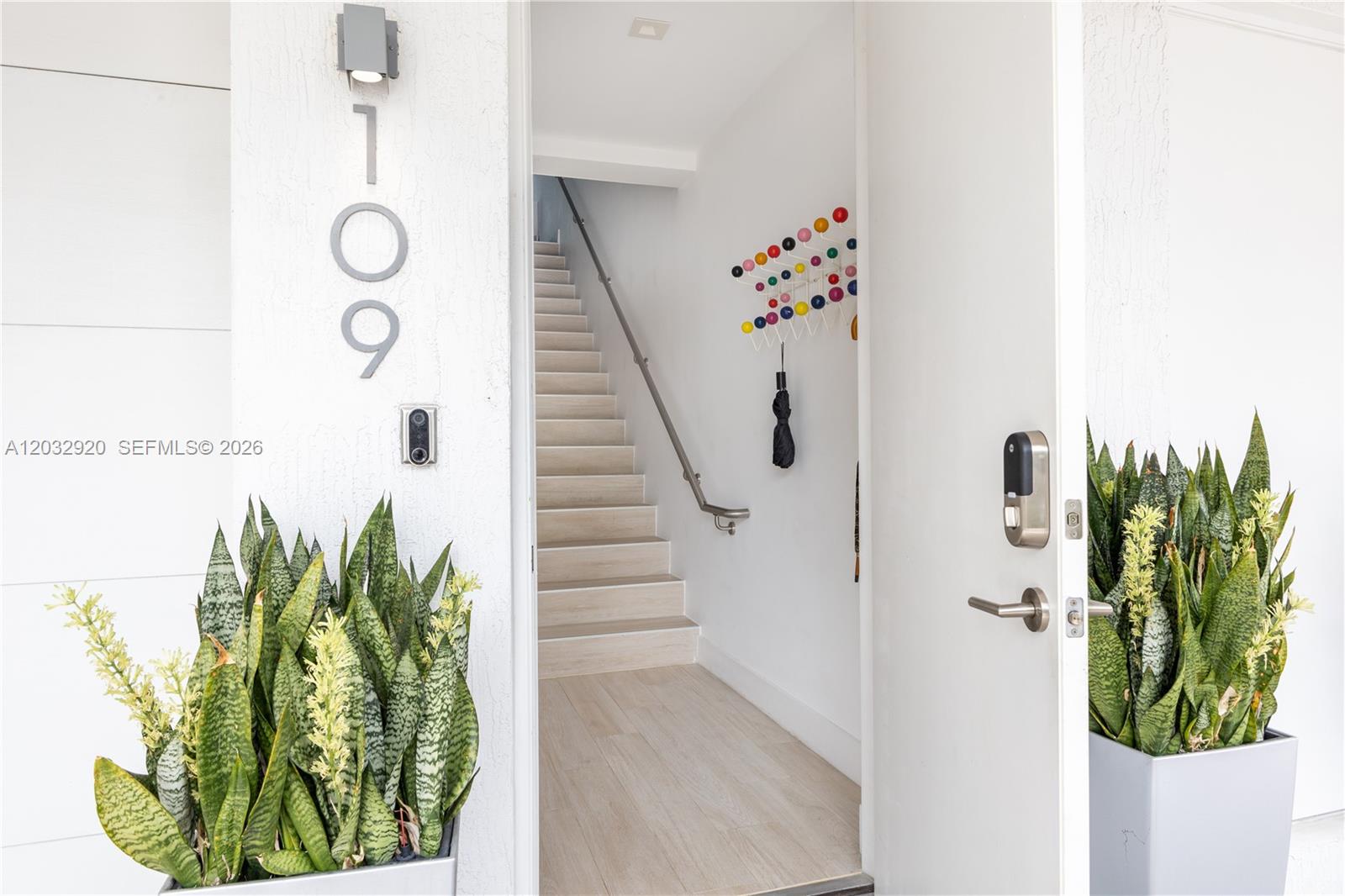 An open front door reveals a staircase with light wood flooring and a colorful coat rack — 455 NE 39th St # 109, Miami FL 33137, MIAMI, FL