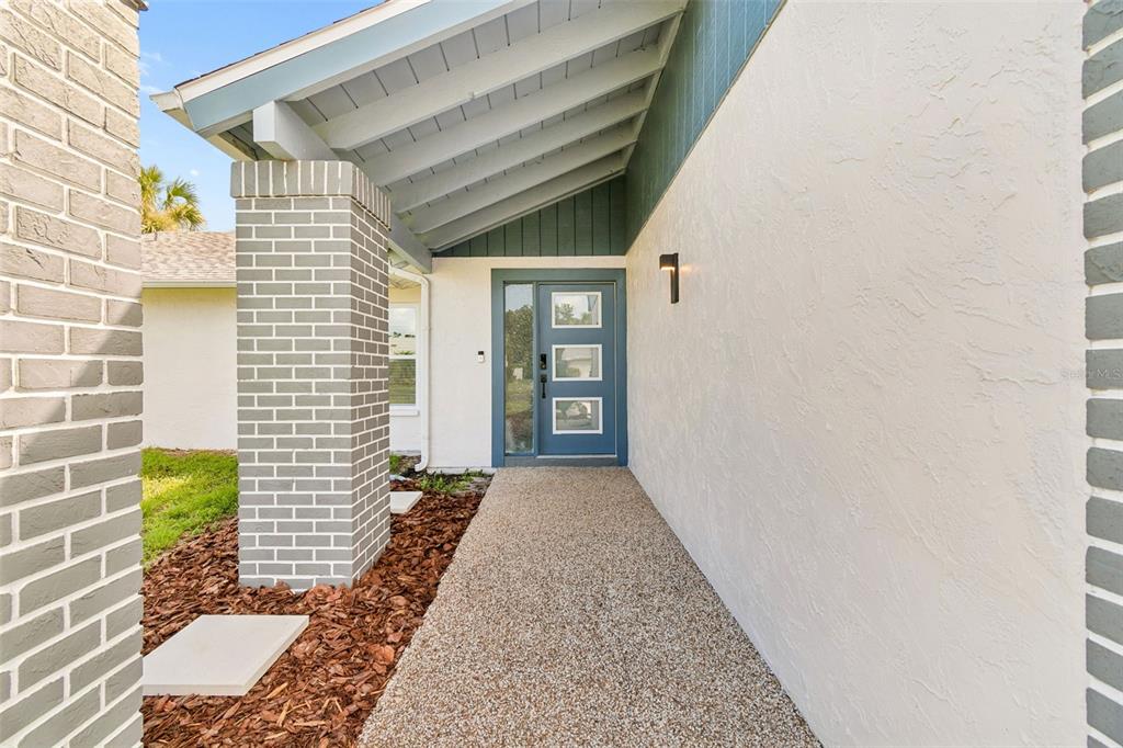 A front entryway features a blue door with three windows, a brick pillar, and stucco — 4559 INGERSOL PLACE, NEW PORT RICHEY, FL