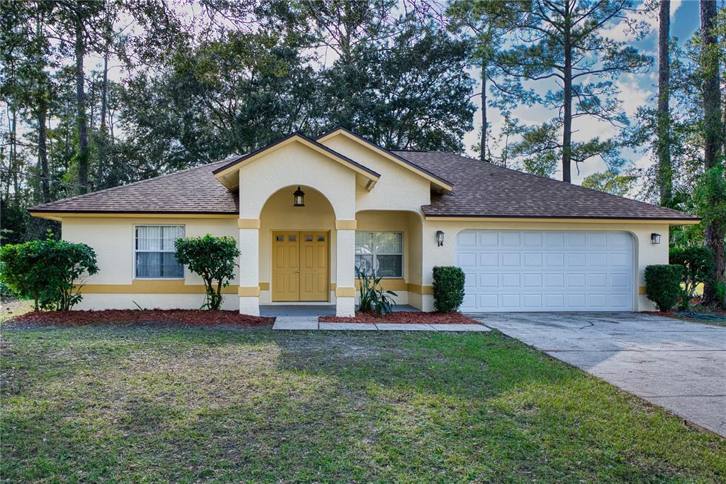 A single-story house with a yellow exterior, arched entryway, double front doors, and two-car garage — 14 WELLSHIRE LANE, PALM COAST, FL