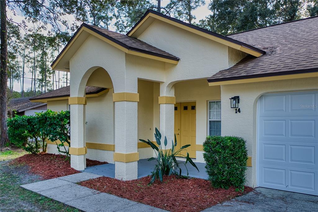 A single-story house exterior features a yellow front door, arched entryway, and attached garage — 14 WELLSHIRE LANE, PALM COAST, FL
