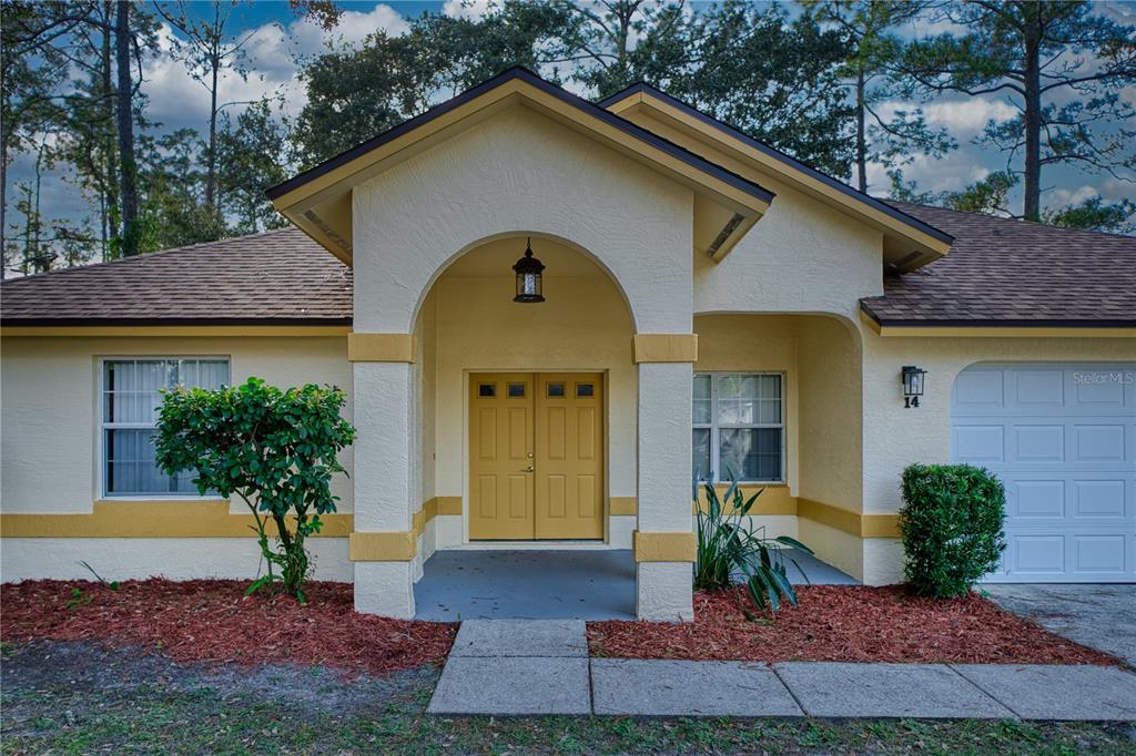 A single-story house with a yellow double front door, arched entryway, and a garage — 14 WELLSHIRE LANE, PALM COAST, FL